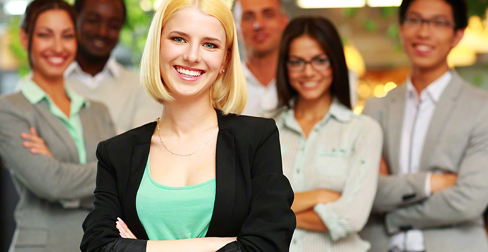 Cheerful businesswoman with arms folded standing in front her colleagues