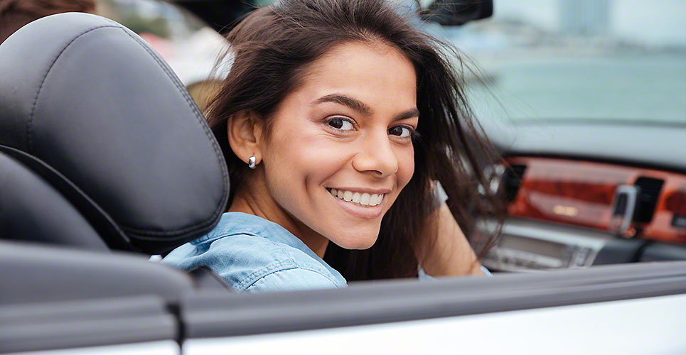 Smiling young woman sitting inside her convertible car